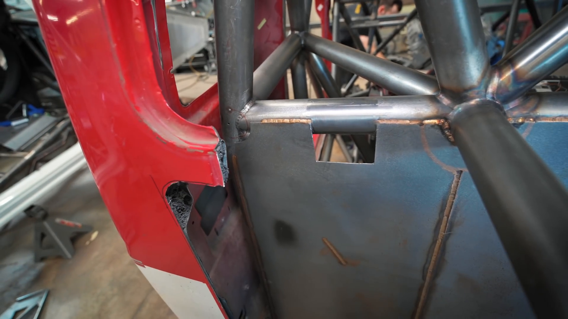 Close-up of a Prerunner roll cage under construction inside a red vehicle body with visible welds on metal tubes and panels.